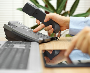 hand touching office phone and tablet on desk